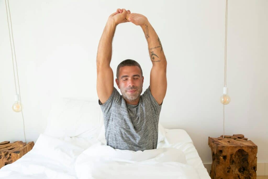 Man sitting up stretching in bed.