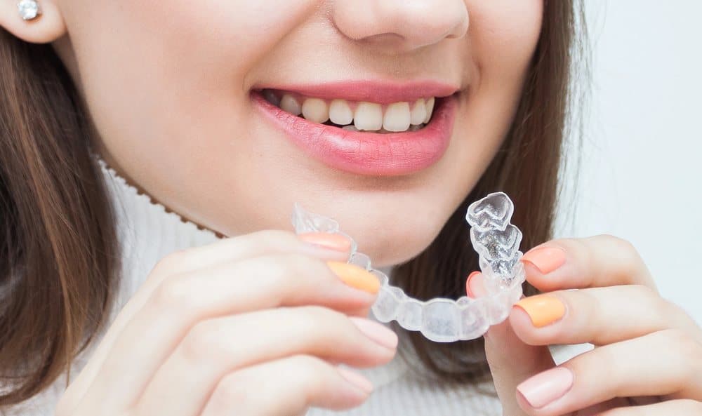 A woman smiling while holding clear aligners before placing them on her teeth, representing orthodontic treatment in Auckland.