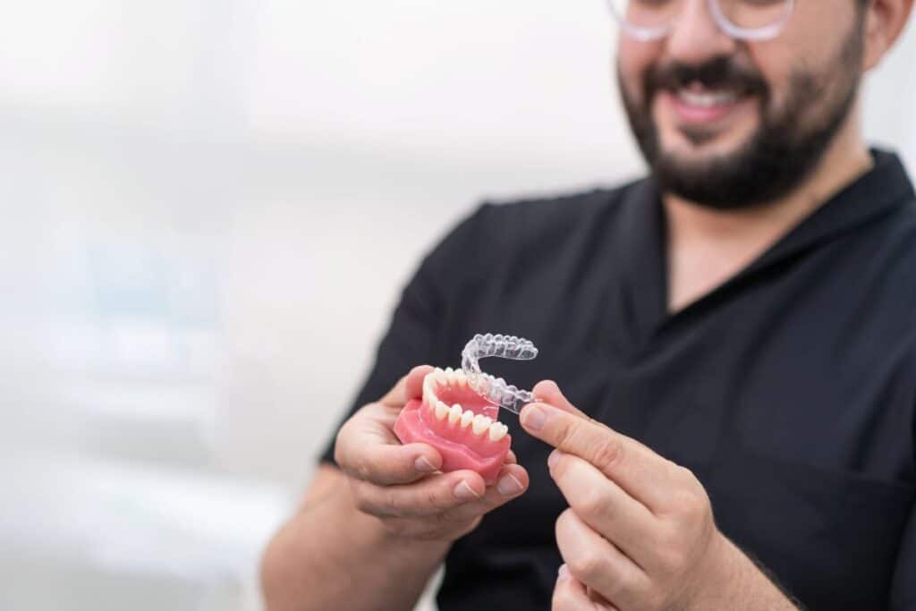 An orthodontist holding a clear aligner over a dental model, explaining refinement adjustments for clear aligner treatment.