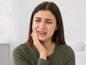 A girl with braces in a green shirt holding onto her check and wincing in pain